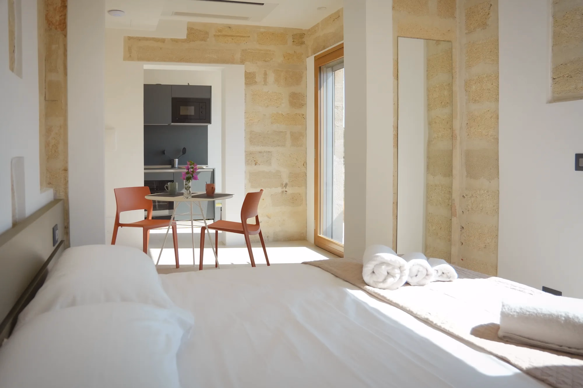 La dimora Cala Grande, il letto e il tavolo da pranzo davanti alla parete di calcarenite a vista