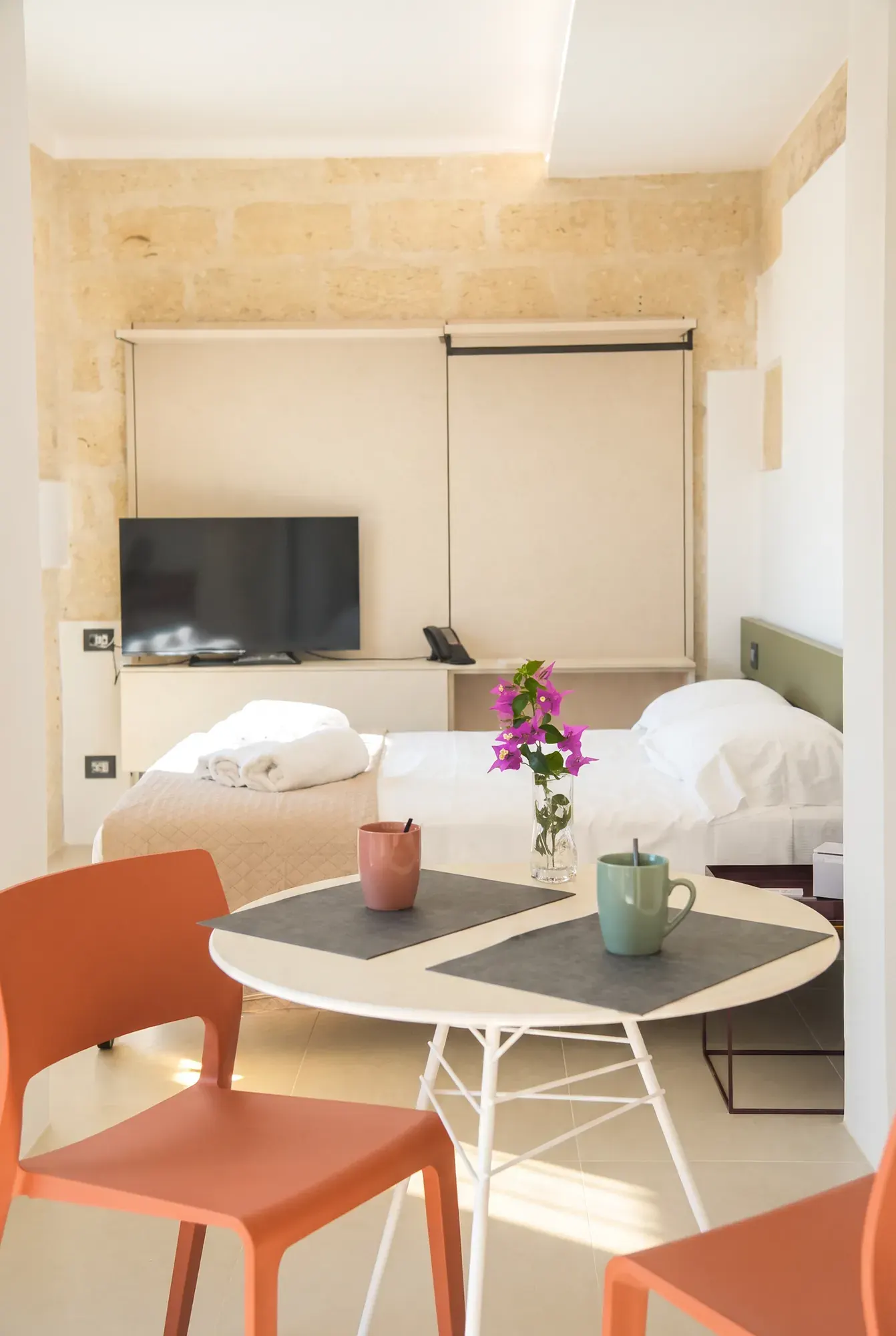 The living area at Cala Grande, the round table with orange chairs in front of the bed and the calcarenite wall