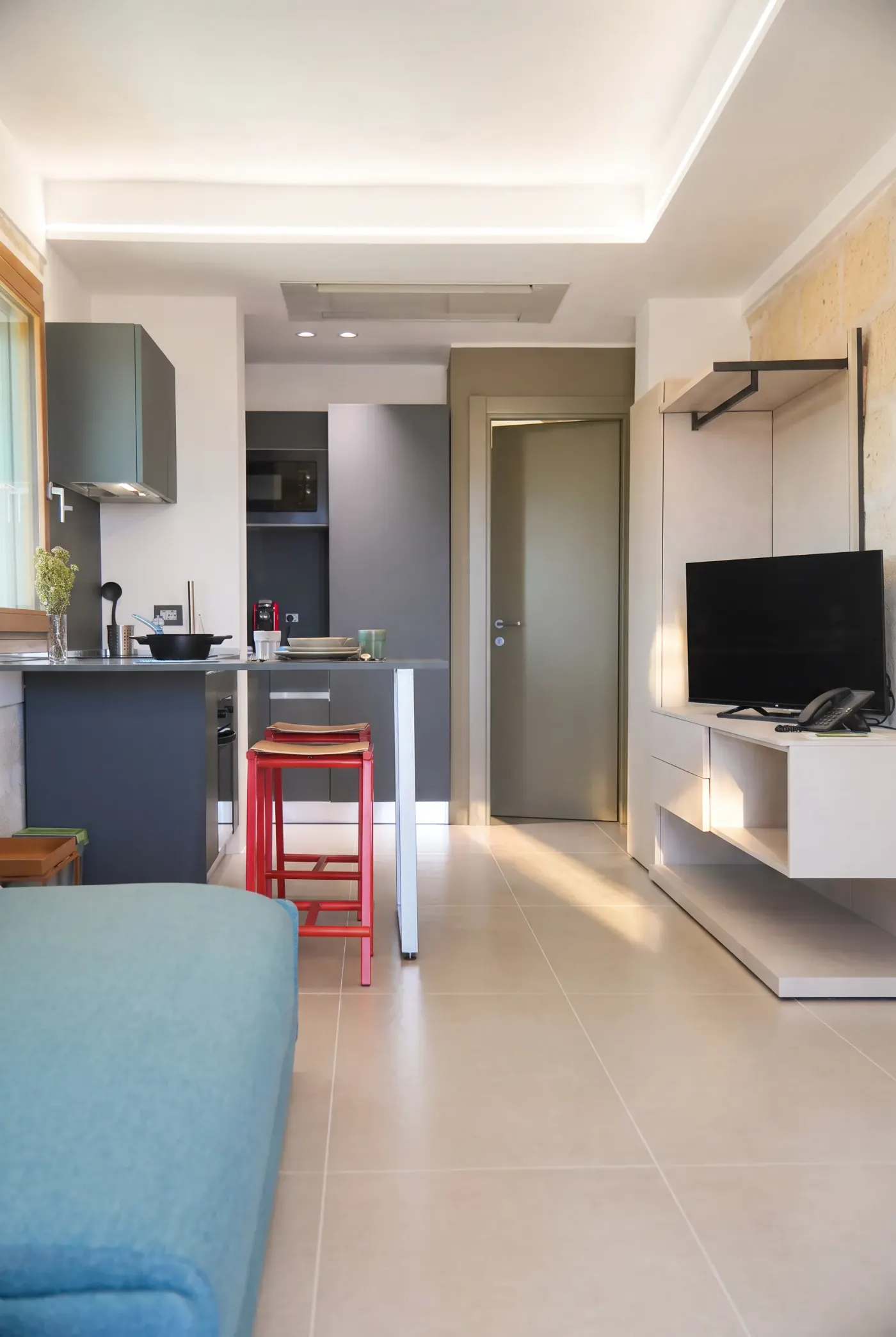 La zona giorno di Lo Scivolo, cucina, tavolo alto e divano sotto la parete di calcarenite