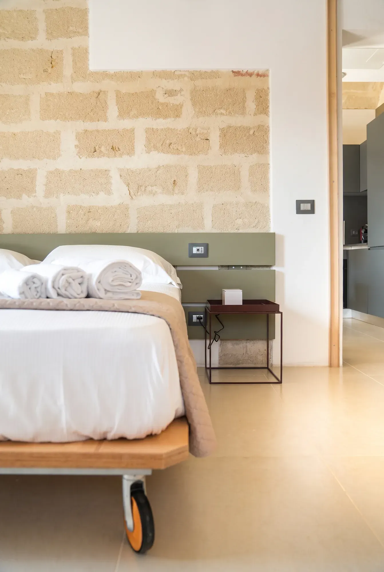 Il letto di Pirreca con la testiera verde salvia, appoggiato alla parete di calcarenite