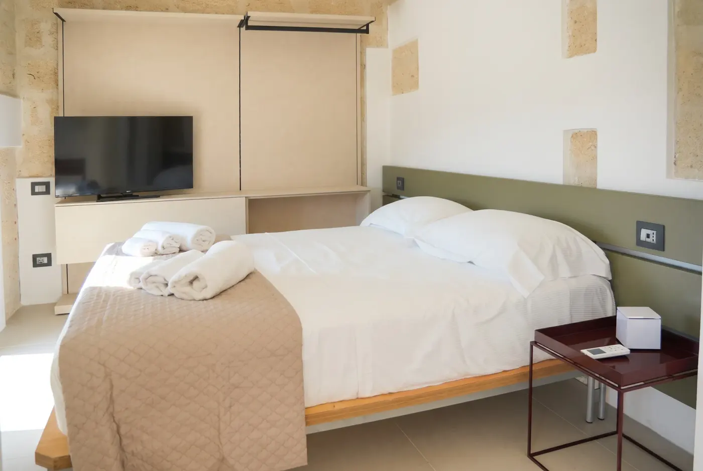 The double bed at Cala Grande, sage green headboard and fitted wall unit with television