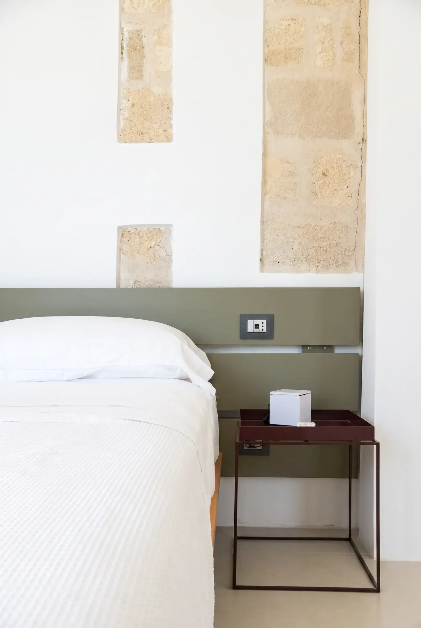 The side of the bed at Cala Grande, the red side table and the exposed calcarenite wall