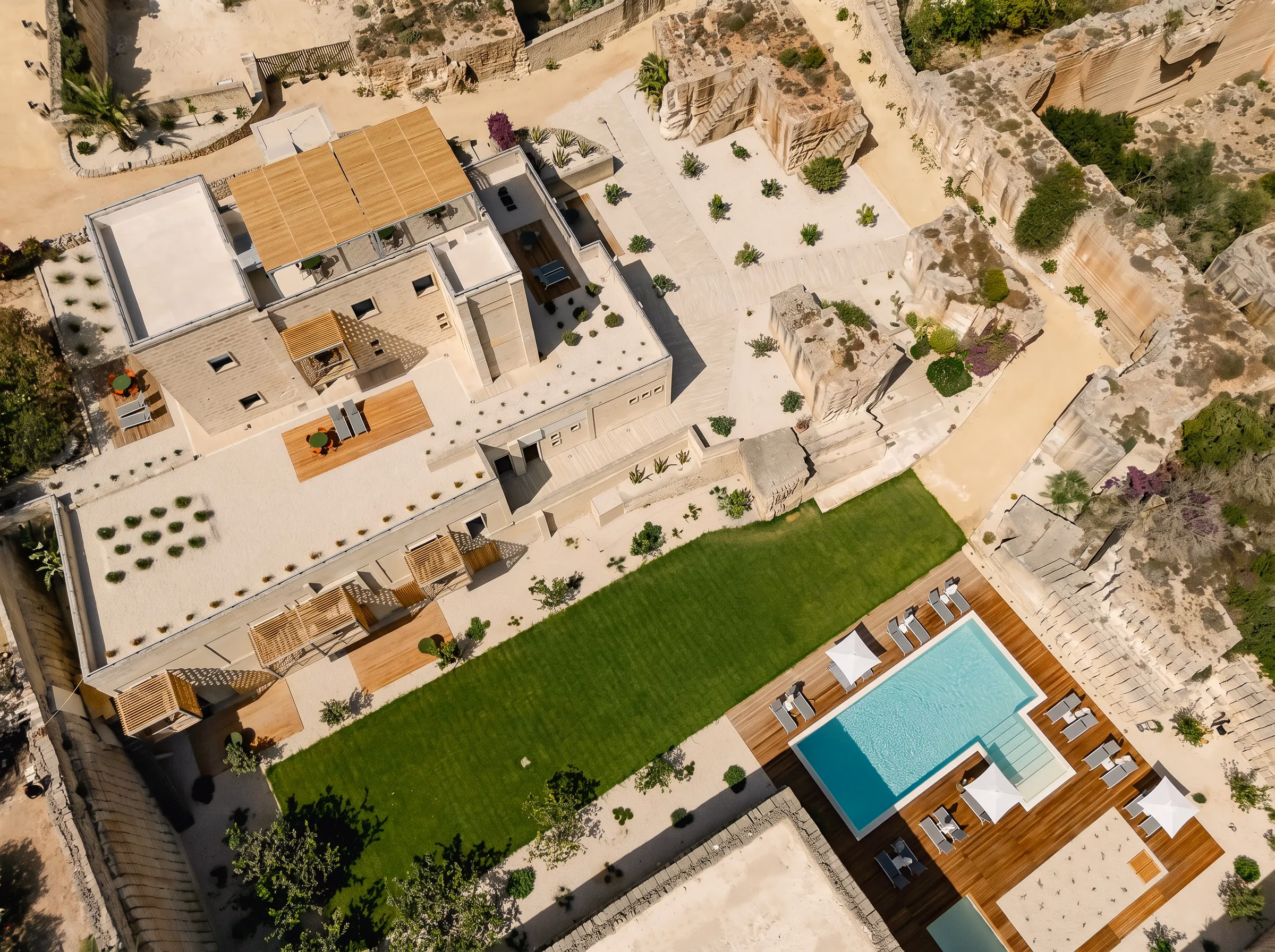Vista zenitale di Pirrera: i tetti, i terrazzi in legno, il prato e la piscina sul fondo
