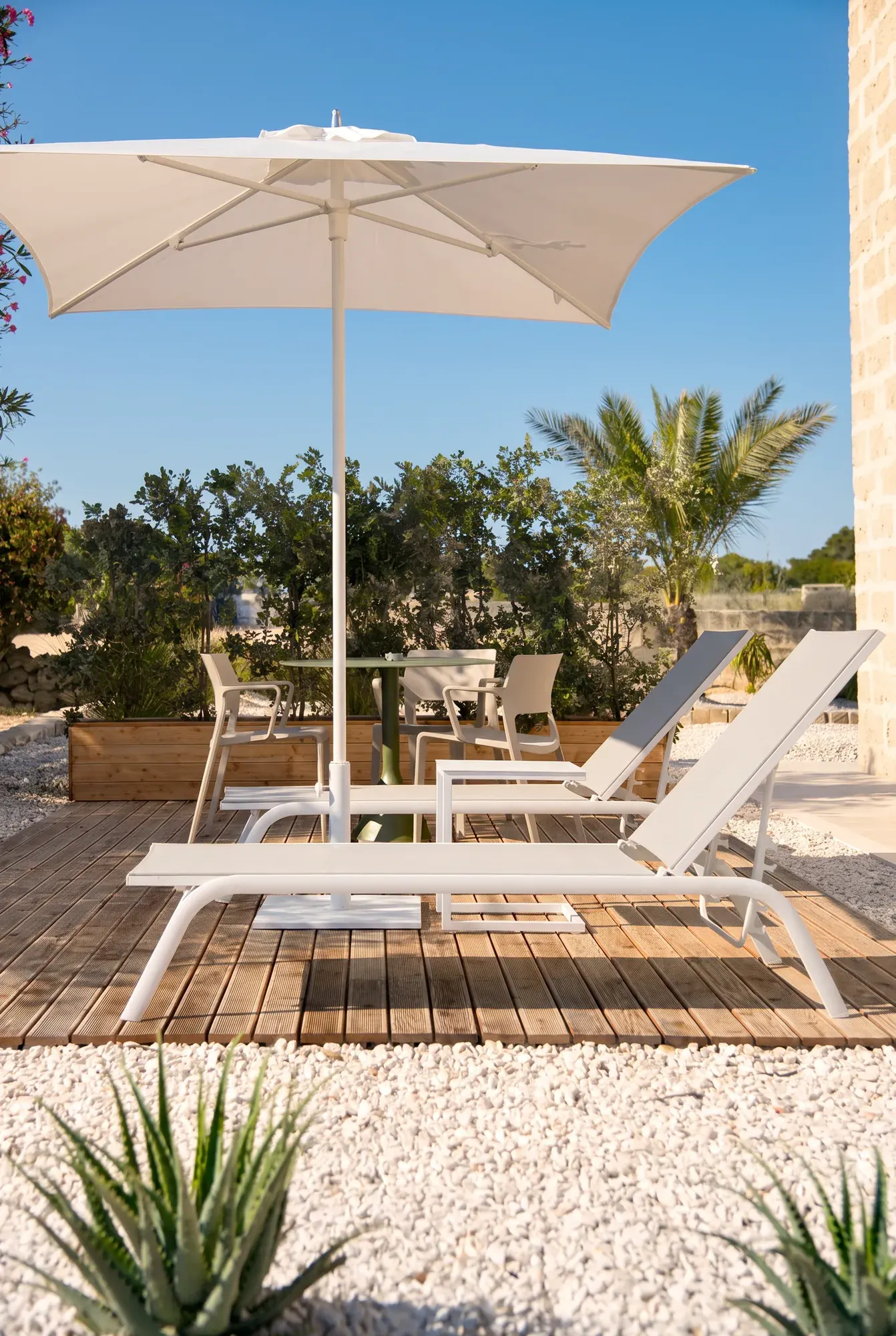 Il deck di Pirreca con lettini e ombrellone, l'aloe sulla ghiaia bianca in primo piano